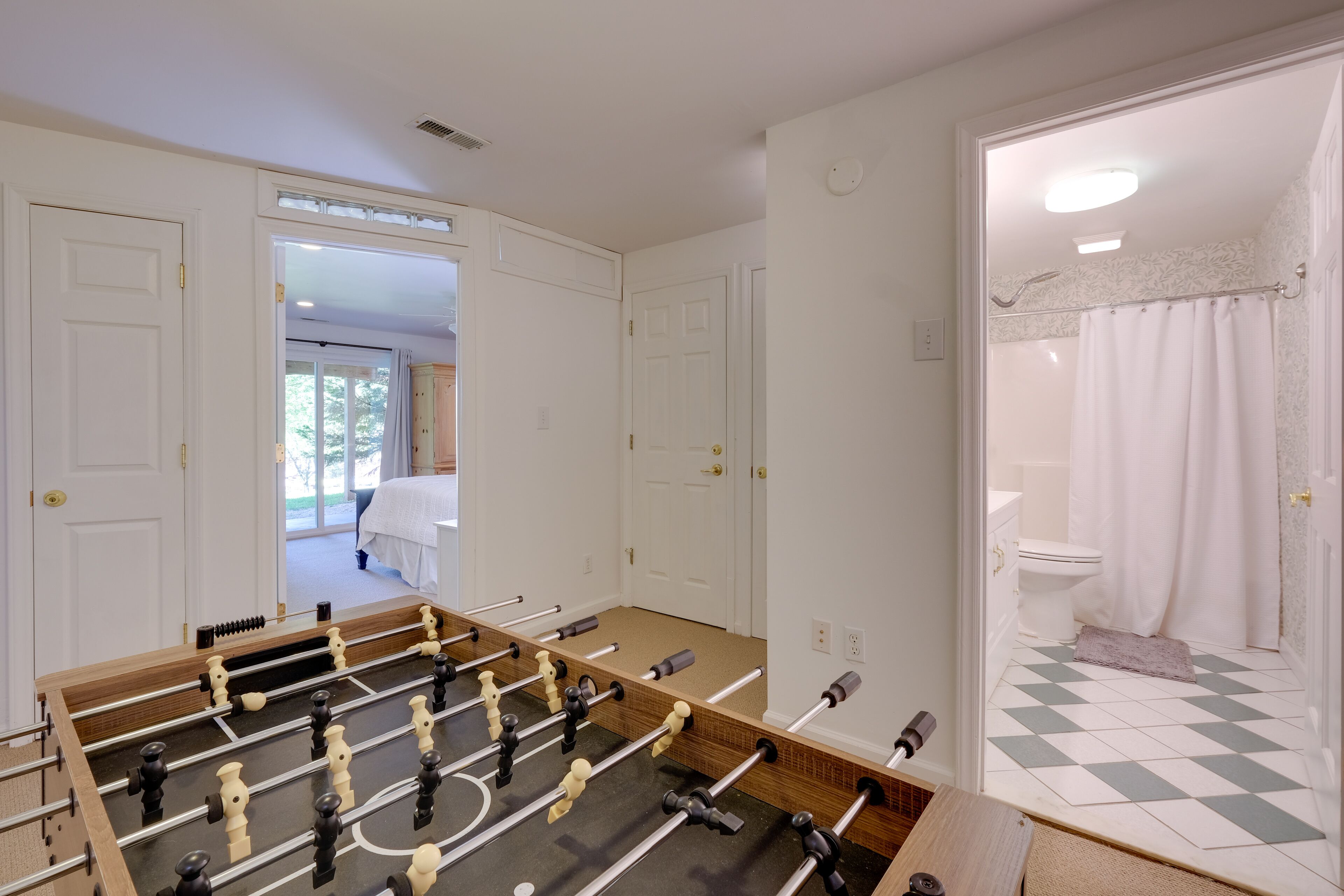 A room with a foosball table, a bathroom with a shower, and a door leading to another room.