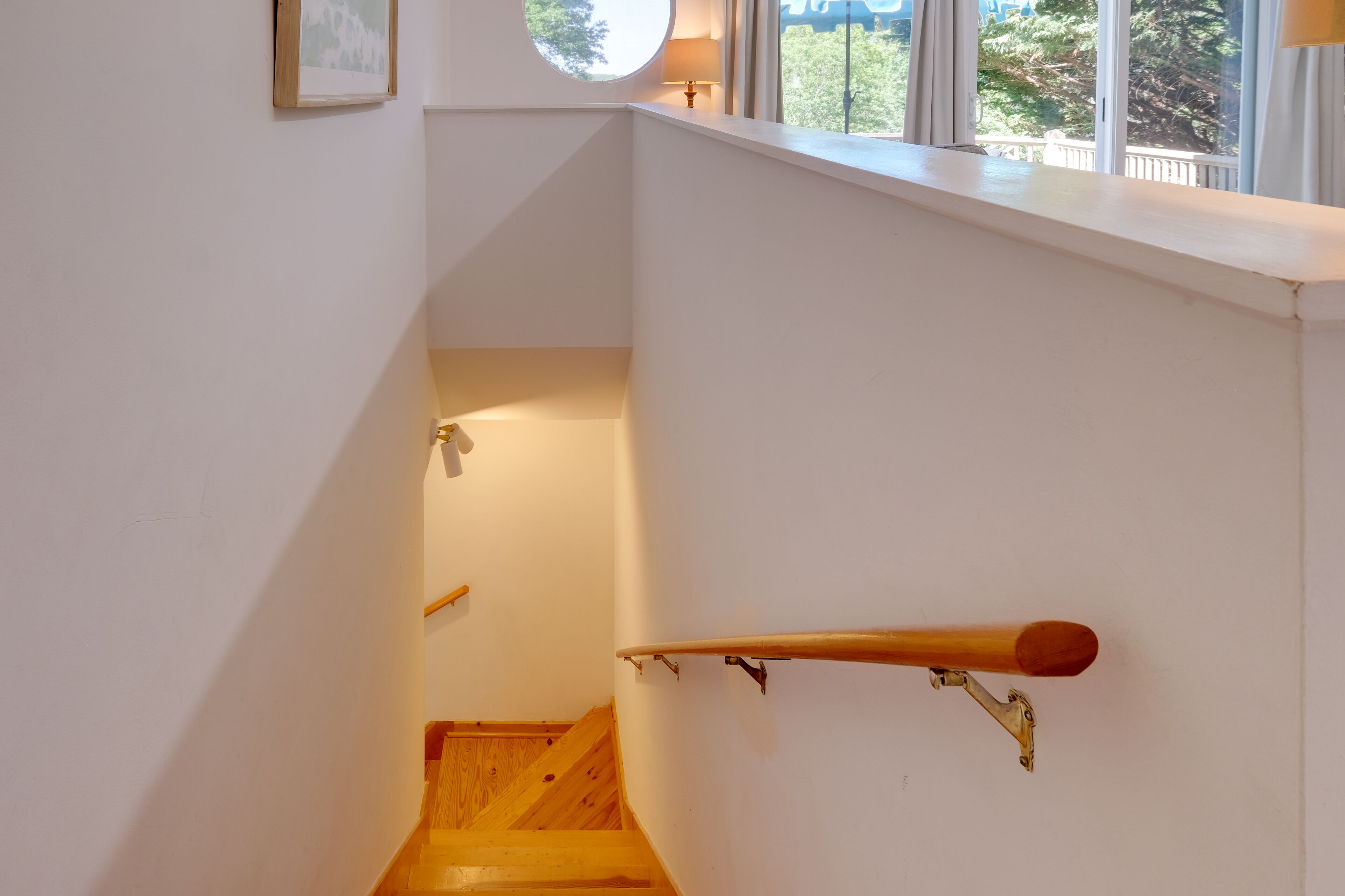A staircase with wooden steps and a handrail, leading to a landing with a window and a lamp.