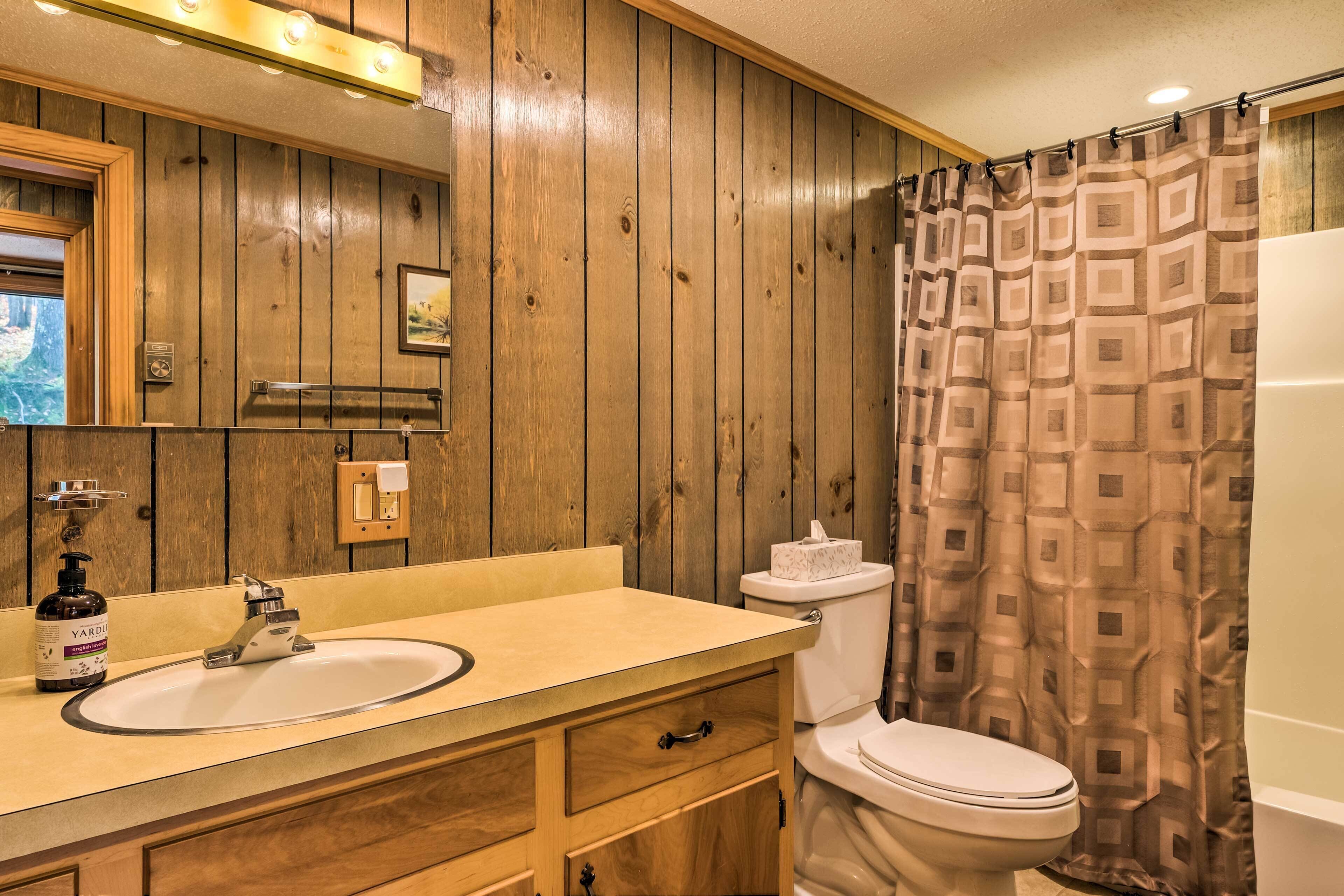 A bathroom with wooden paneling, a sink with a bottle of Yardley soap, a toilet, and a shower curtain with a geometric pattern.