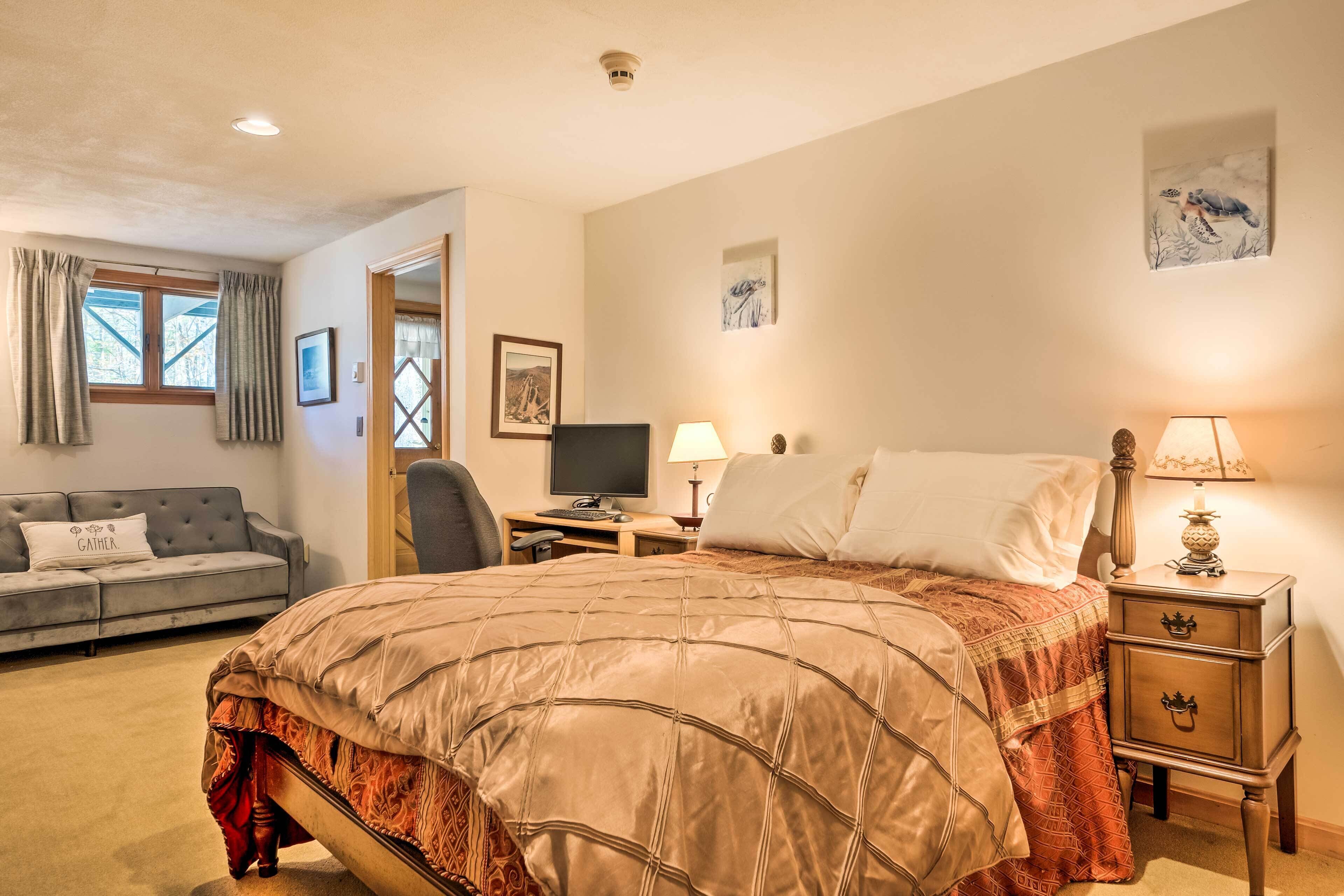 A bedroom with a large bed, a desk with a computer, a chair, a small table with a lamp, and a couch.