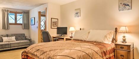 A bedroom with a large bed, a desk with a computer, a chair, a small table with a lamp, and a couch.