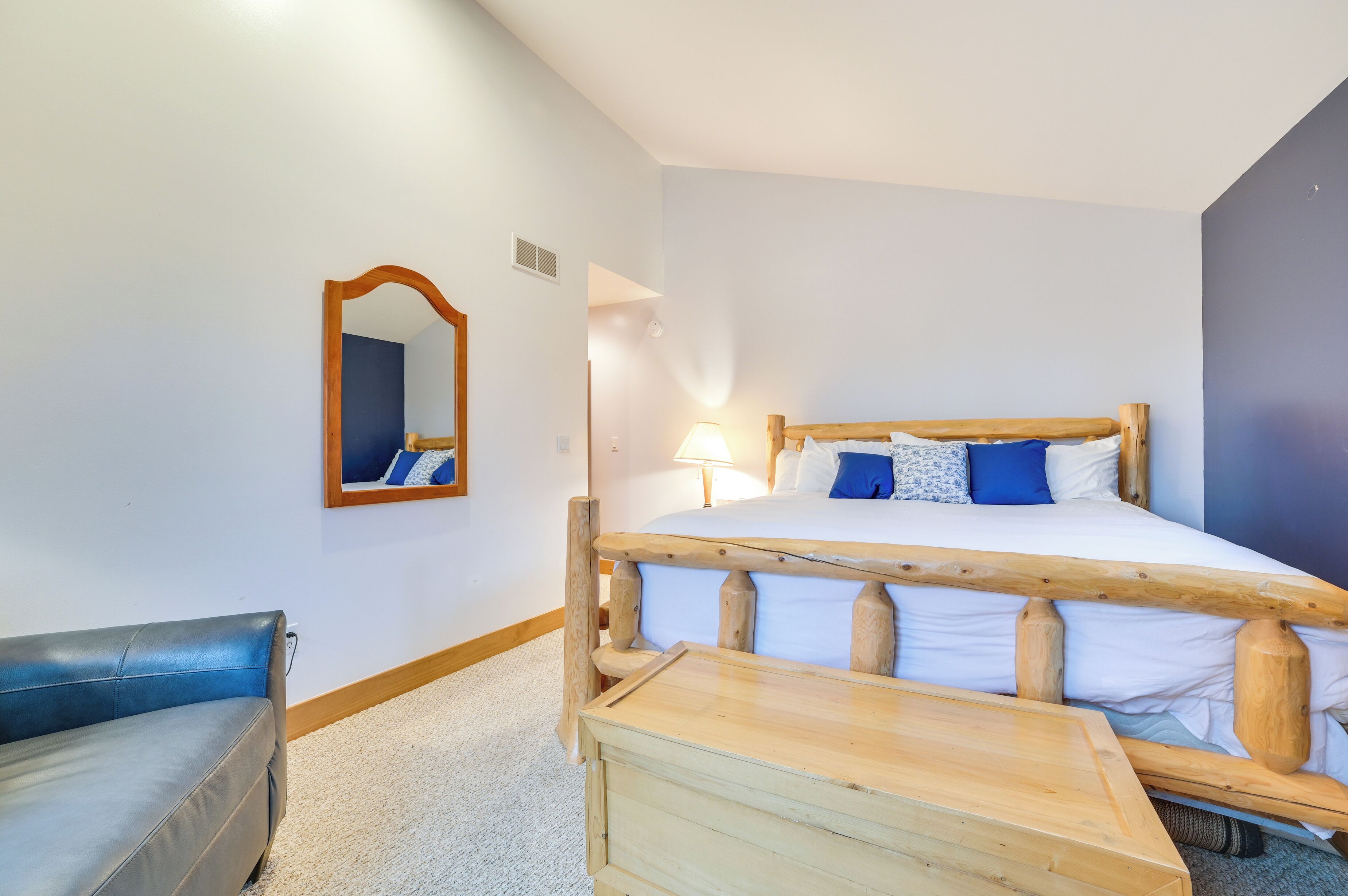 Una camera da letto con un letto di legno, un divano blu, un comodino in legno e uno specchio sulla parete.