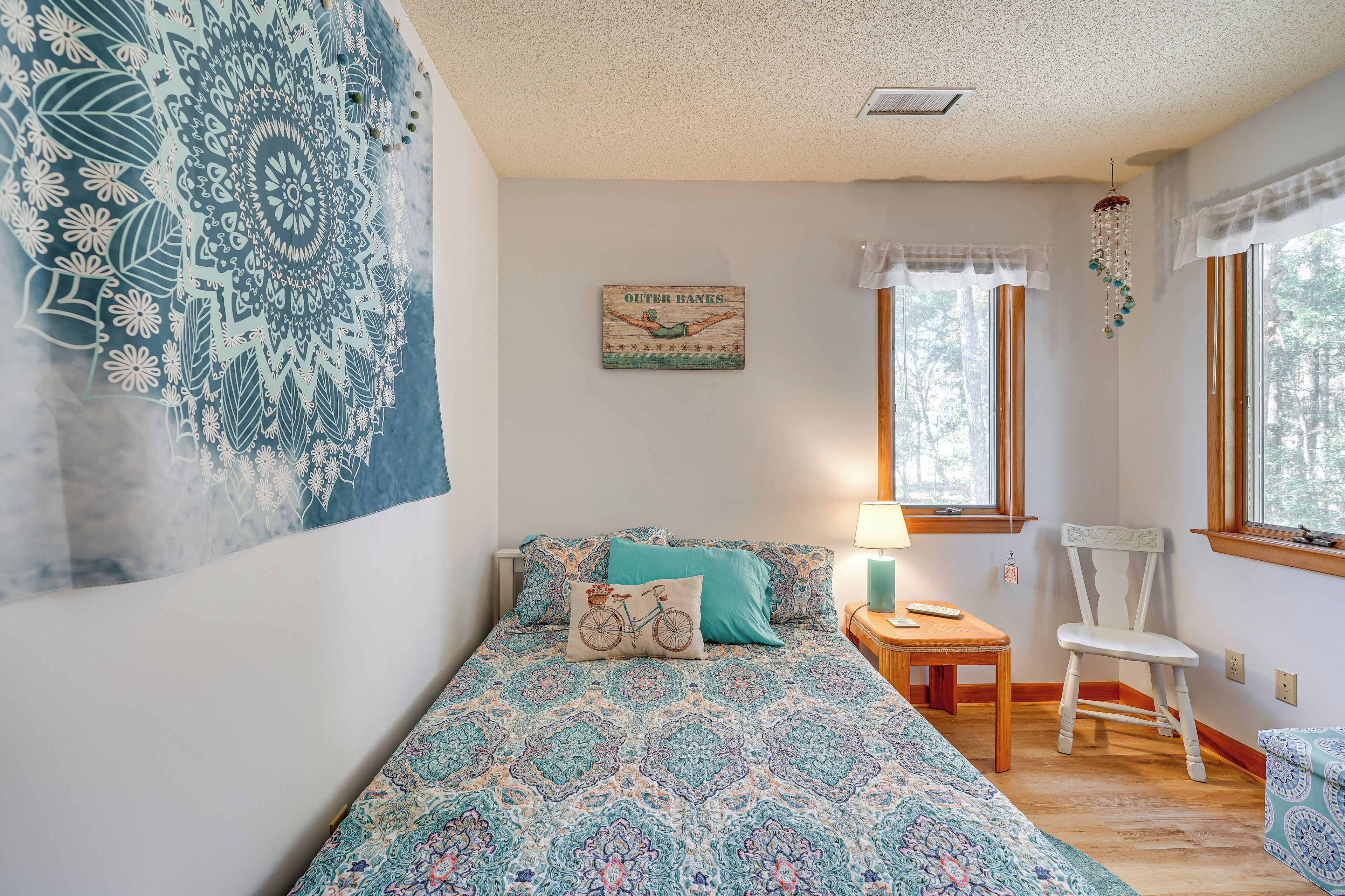 A bedroom with a patterned bedspread, a bicycle pillow, a chair, and a wall-mounted artwork.
