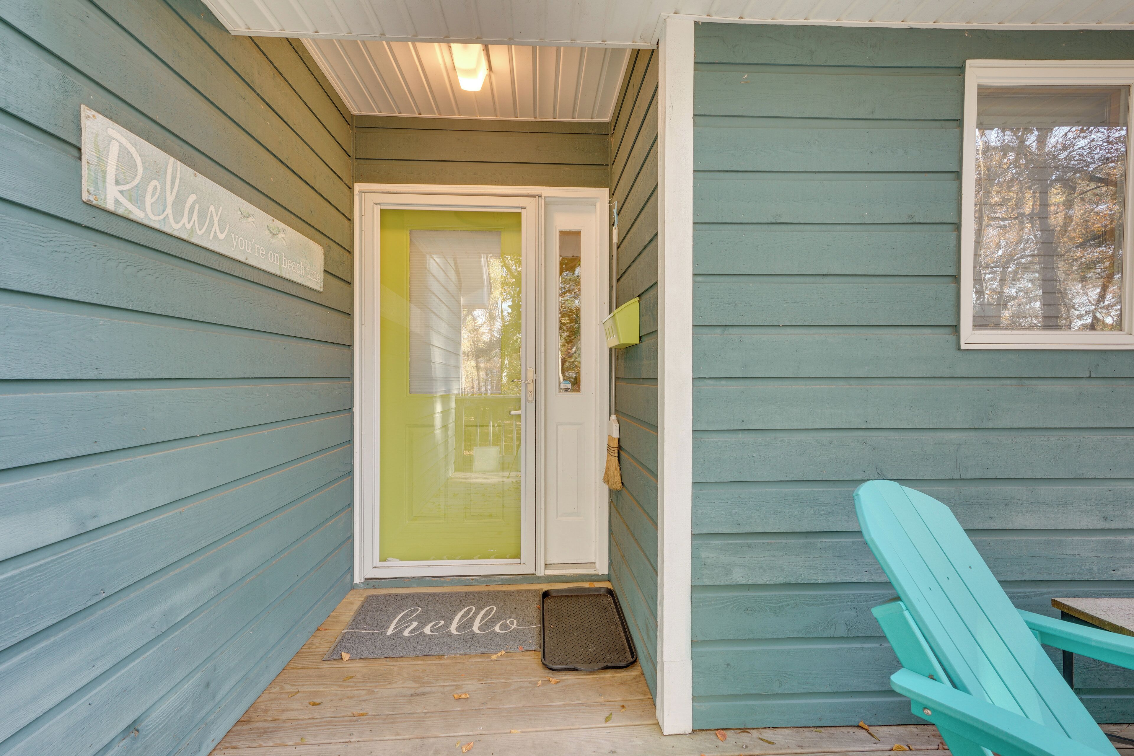 A wooden porch with a teal-colored chair, a door with a glass panel, and a 'Relax' sign on the wall.