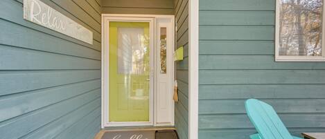 A wooden porch with a teal-colored chair, a door with a glass panel, and a 'Relax' sign on the wall.