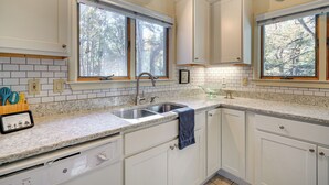 Una cocina con armarios blancos, un lavamanos doble y una ventana con vistas a árboles.