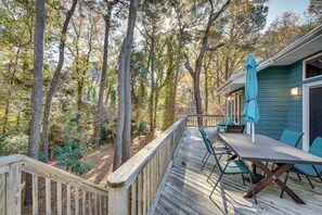 A wooden deck with a table and chairs, surrounded by trees. - 1/2 Mi to Beach Access: Southern Shores Gem + Deck (Kitty Hawk)