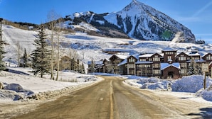 A snow-covered road leading to a lodge with multiple buildings, a mountain backdrop, and a speed limit sign. - Cozy Crested Butte Condo - Walk to Ski Lift! (Crested Butte)