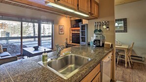 A kitchen with granite countertops, stainless steel sink, wooden cabinets, and a dining area with a table and chairs. - Cozy Crested Butte Condo - Walk to Ski Lift! (Crested Butte)
