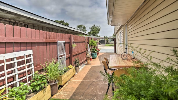 A covered outdoor patio with a wooden table and chairs, surrounded by potted plants and a red wooden fence. - Apartment w/ Patio: 15 Miles to French Quarter! (Westwego)