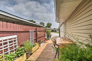 A covered outdoor patio with a wooden table and chairs, surrounded by potted plants and a red wooden fence. - Apartment w/ Patio: 15 Miles to French Quarter! (Westwego)