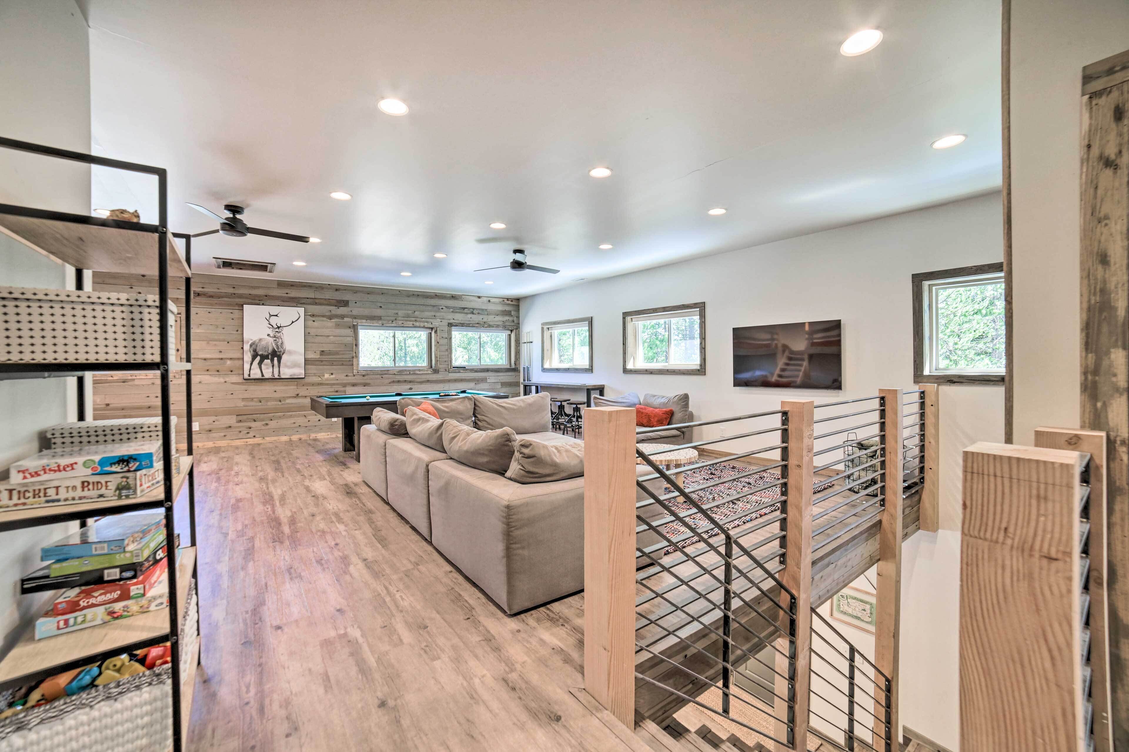 A spacious living area with a sofa, a pool table, and a ceiling fan. There are windows and a wooden wall with a deer painting.