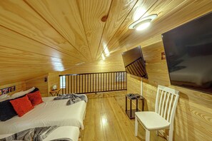 Ein Zimmer mit einem Bett, einem Sessel, einem an der Wand montierten Fernseher und einem Fenster.