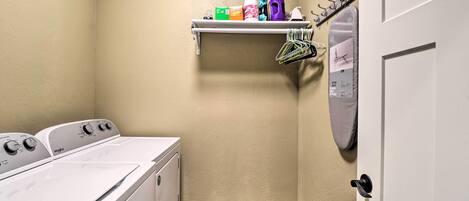 A laundry room with a washing machine, dryer, and a shelf with cleaning supplies.