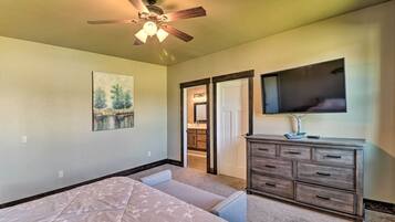 Ein Schlafzimmer mit Bett, Schminktisch, Deckenventilator, Gemälde und Fernseher an der Wand.