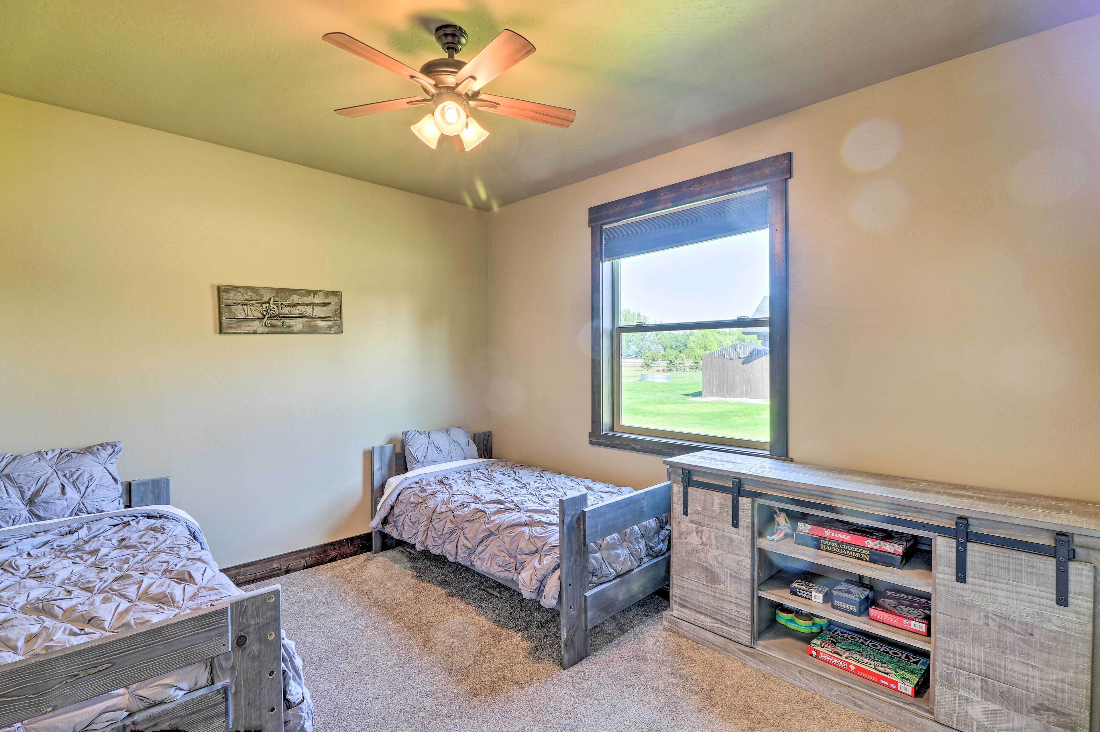 A bedroom with two beds, a ceiling fan, a window with a view, and a built-in bookshelf with board games.