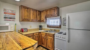 A kitchen with wooden cabinets, a white refrigerator, a stove, a microwave, a toaster, and a window with blinds. - Charming Laconia Home w/ Deck: Walk to Lake! (Laconia)