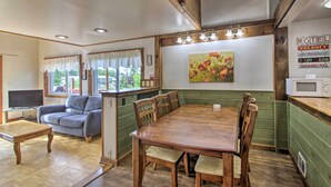 A dining area with a wooden table and chairs, a television, and a sofa in a room with green walls and wooden beams. - Charming Laconia Home w/ Deck: Walk to Lake! (Laconia)