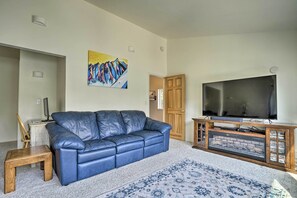 Een woonkamer met een blauwe leren bank, een televisie op een houten standaard, een kleine houten tafel en een kleurrijk schilderij aan de muur.