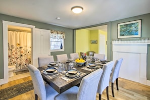 A dining room with a wooden table set for six, surrounded by grey upholstered chairs.