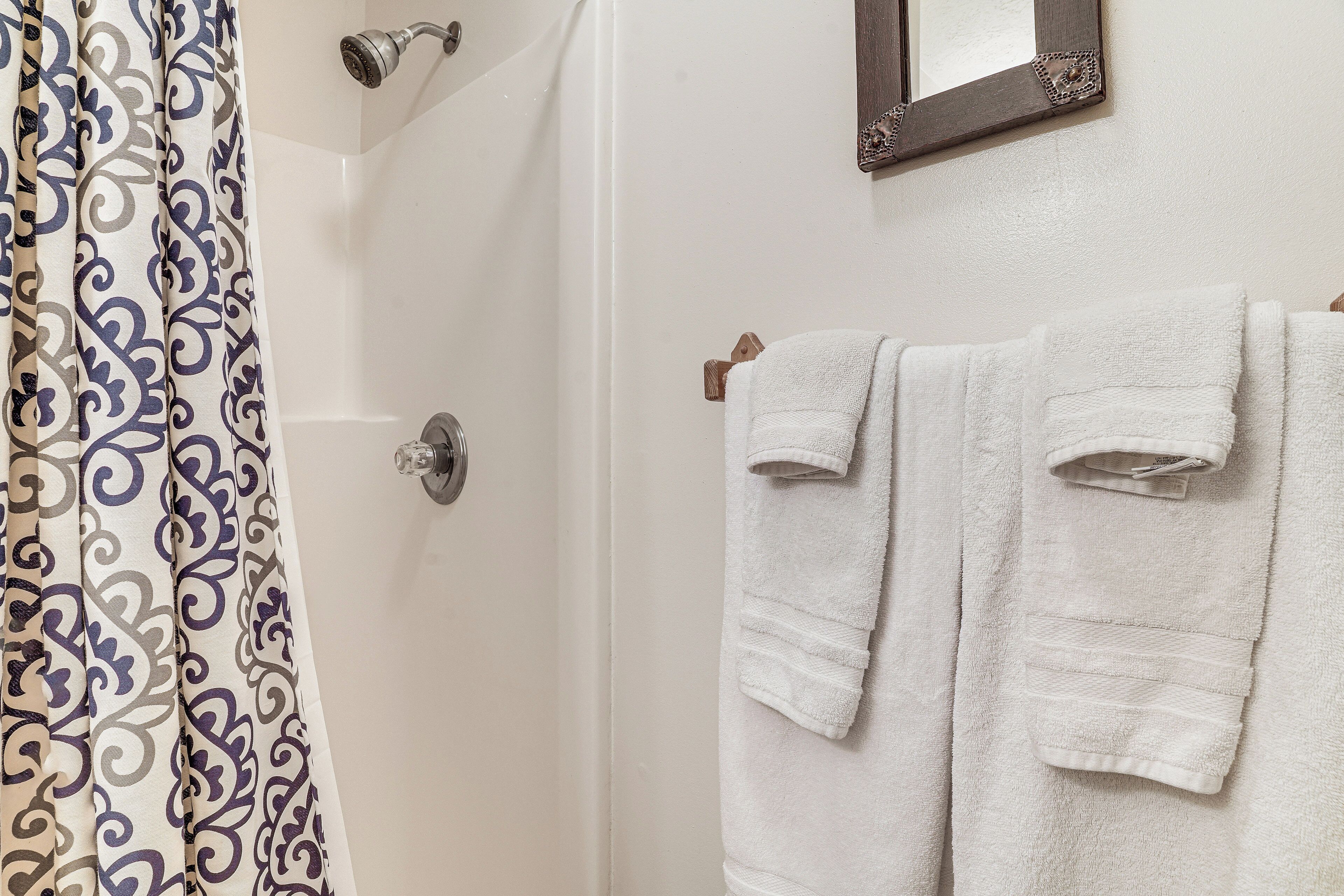 Une salle de bain avec un rideau de douche, un porte-serviettes avec deux serviettes et un miroir au mur.