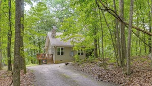A cabin with a gravel driveway, surrounded by tall trees and a wooden deck. - Cabin w/ Deck & Screened-in Porch in New Market! (New Market)