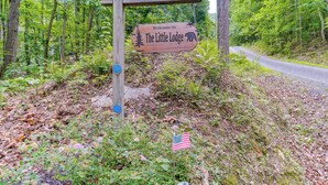 A wooden sign welcoming visitors to The Little Lodge, surrounded by lush greenery and a forested area. - Cabin w/ Deck & Screened-in Porch in New Market! (New Market)