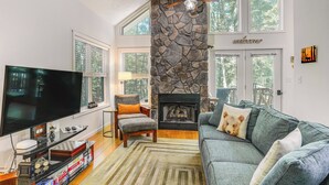 A living room with a stone fireplace, a television, and a cozy seating area. - Cabin w/ Deck & Screened-in Porch in New Market! (New Market)