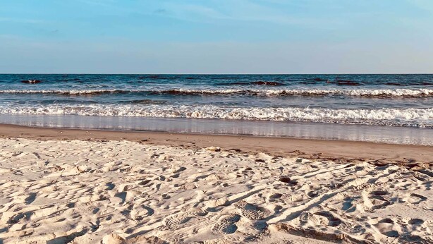 Ein Sandstrand mit Fußspuren, die zum Wasser führen.