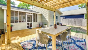 Eine überdachte Terrasse mit Holztisch und -stühlen, einem gemusterten Teppich und einer Holzpergola mit Lichterkette.