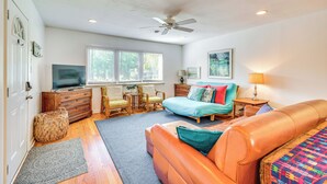 Ein geräumiges Wohnzimmer mit einem großen, orangefarbenen Sofa, einem türkisblauen Bett und einem Deckenventilator.