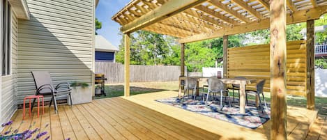 Una terraza de madera con pérgola, mobiliario exterior y vistas a una casa.