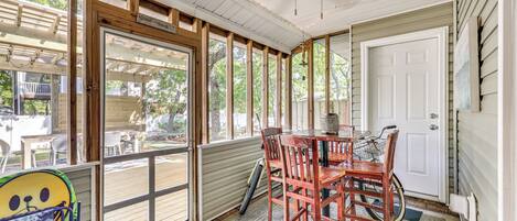 A covered porch with a table and chairs, a door, and a view of the outdoors.