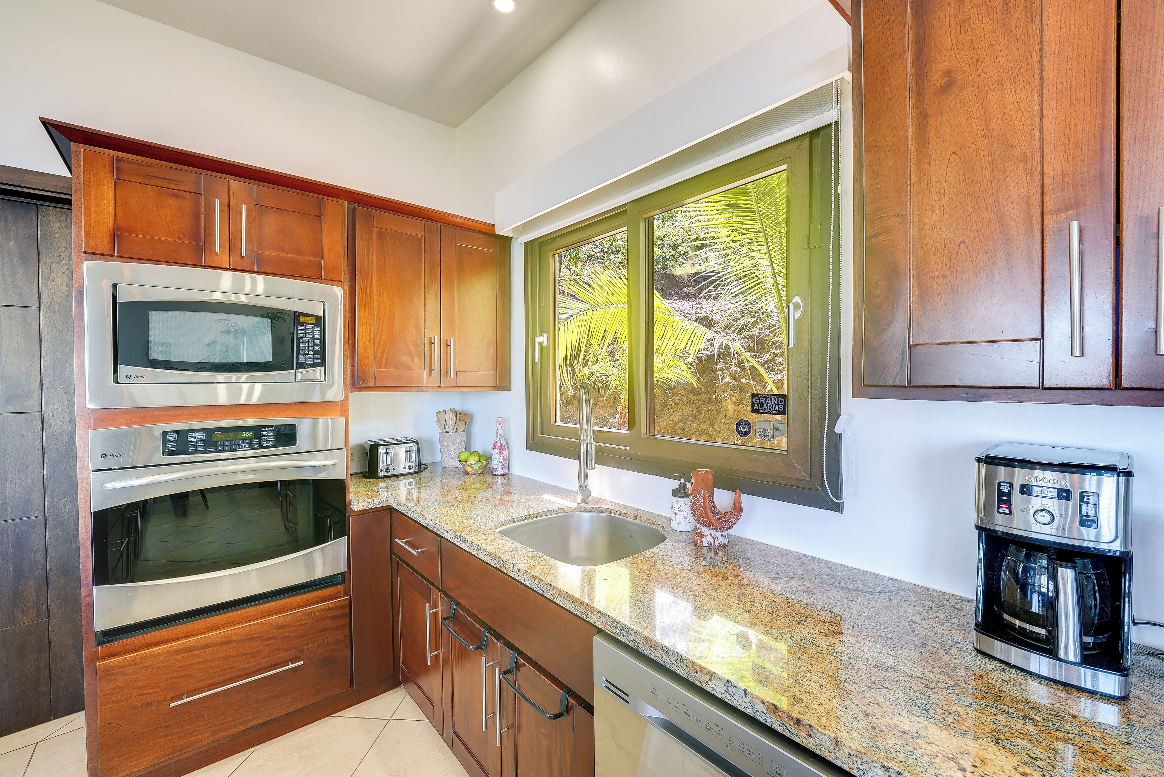Una cocina moderna con electrodomésticos de acero inoxidable, armarios de madera, encimeras de granito y un amplio ventanal con vistas a zonas verdes.
