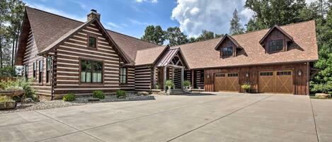 A log cabin with a large driveway, garage, and a covered porch area.