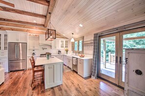 Une cuisine spacieuse avec un plancher en bois, des meubles blancs, un grand îlot central et une vue dégagée sur l’extérieur grâce à une porte vitrée.