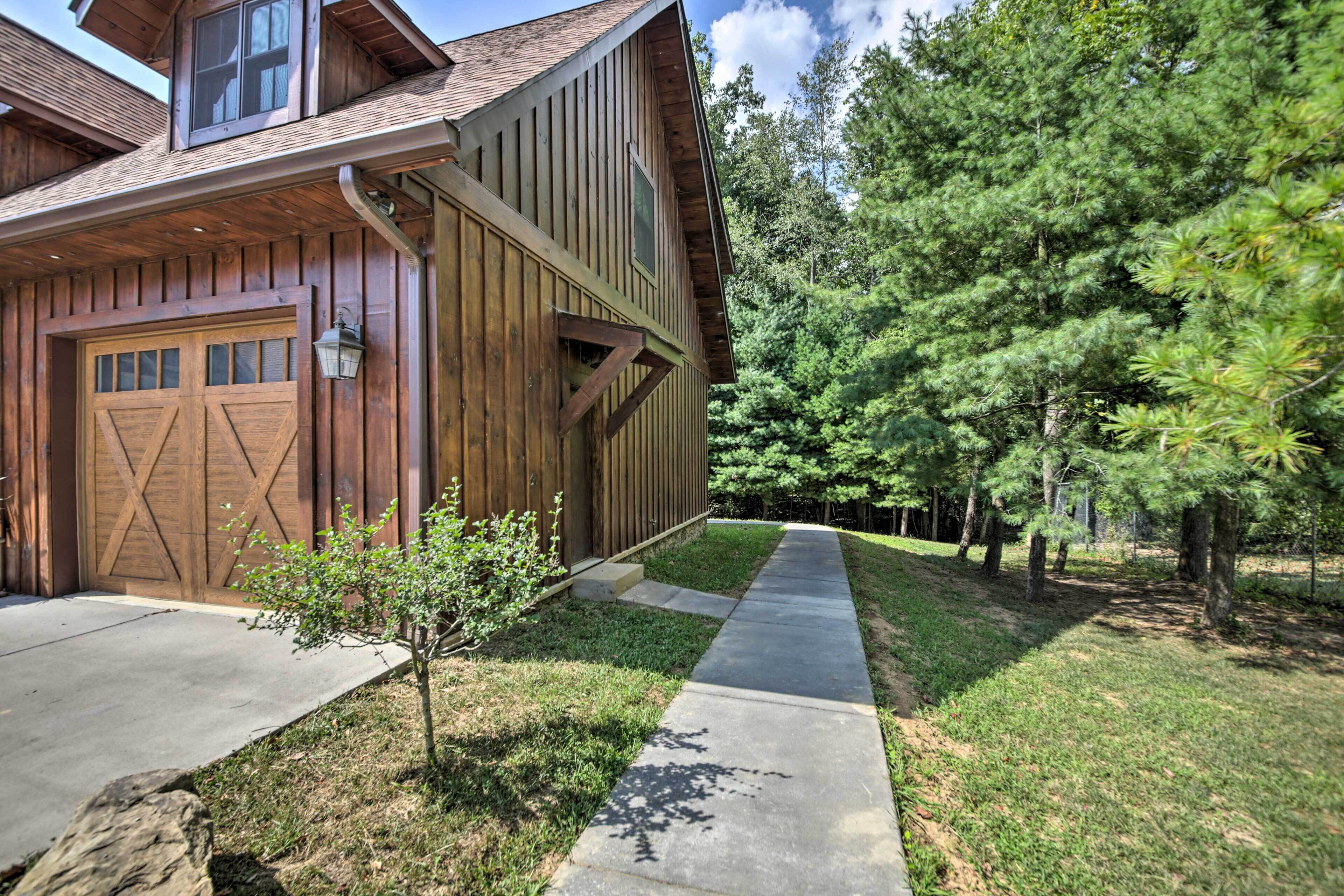 A wooden house with a garage, a small tree, and a concrete pathway.