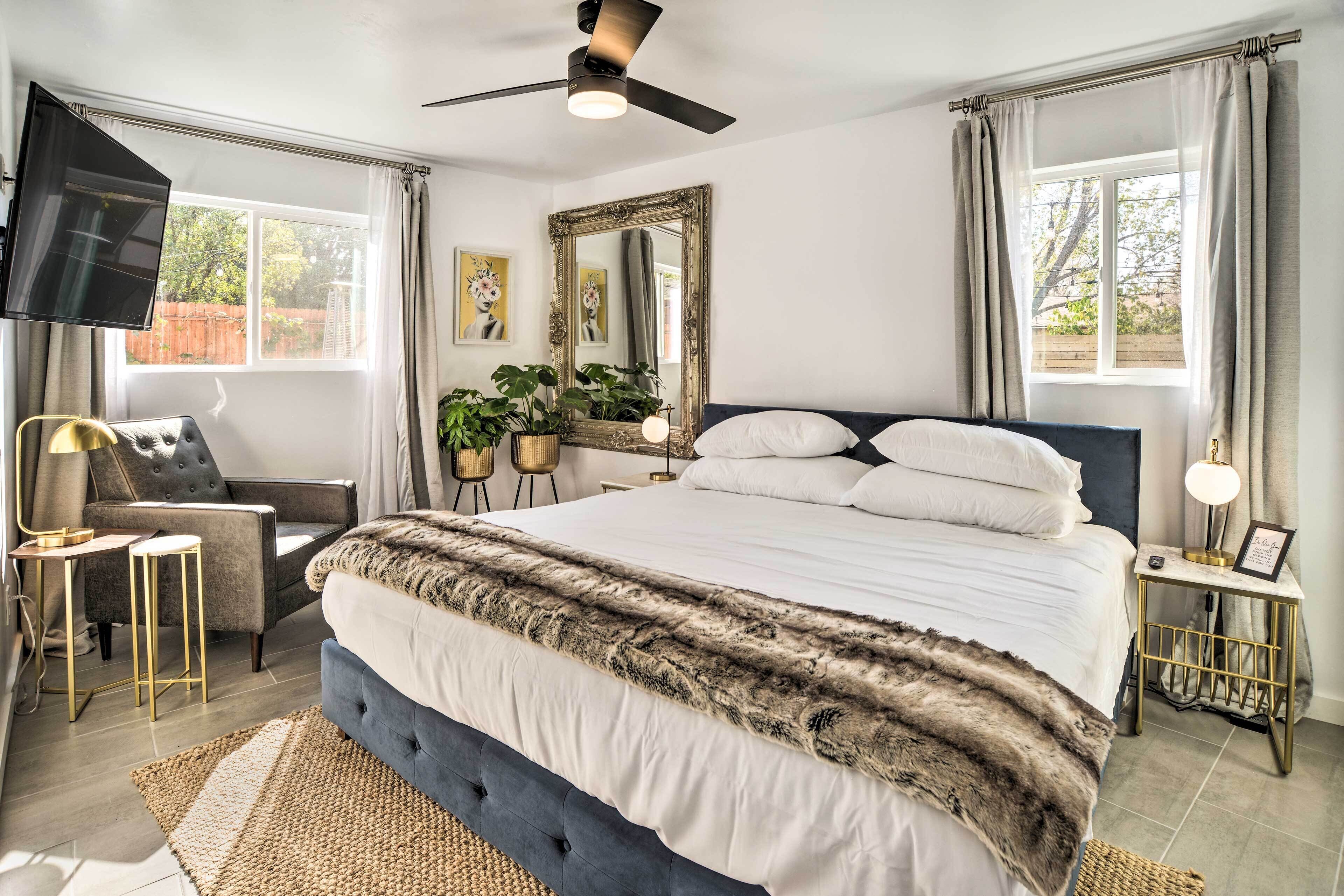 A bedroom with a large bed, a ceiling fan, a TV, and a window with curtains.