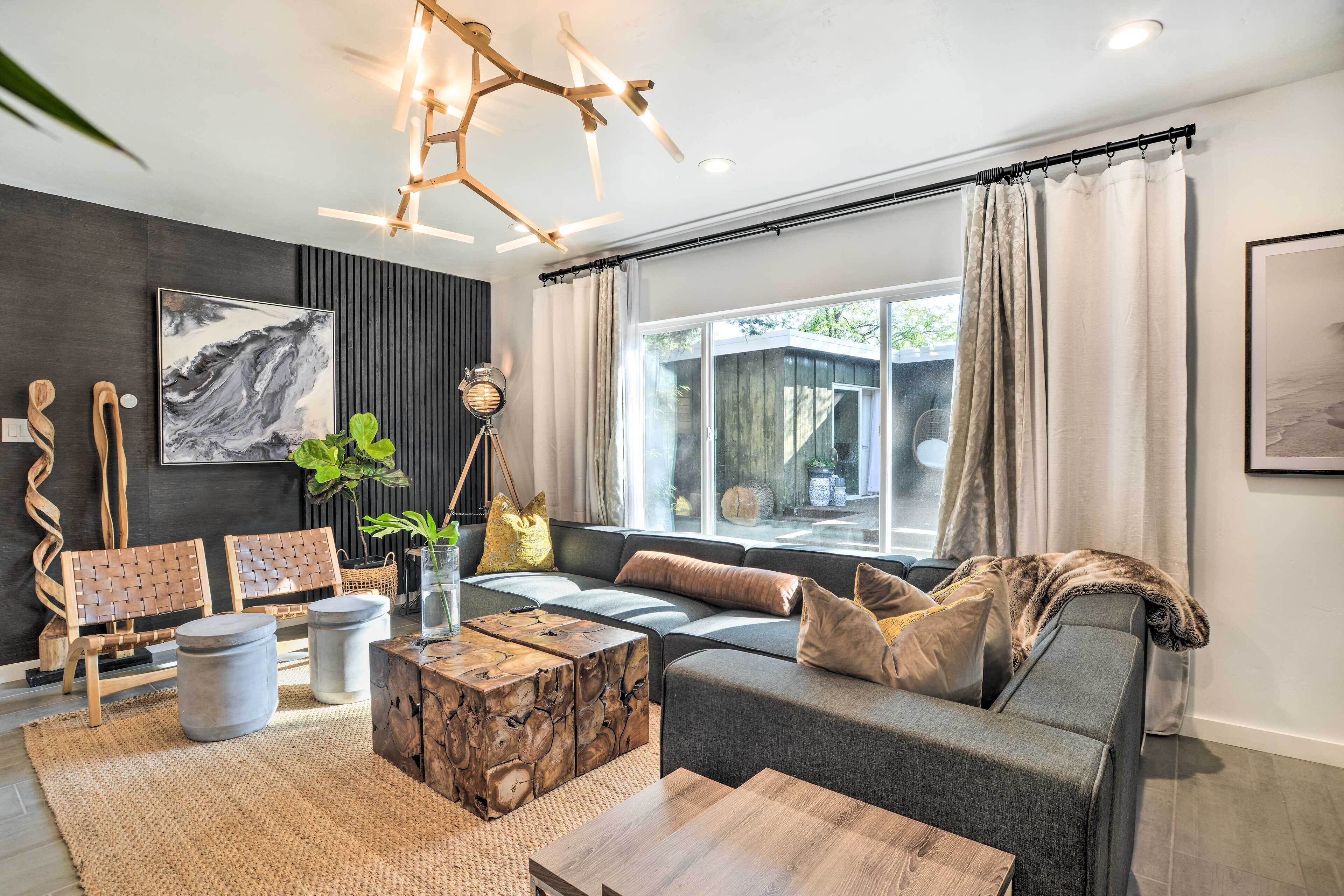 A modern living room with a grey sofa, wooden coffee table, and a large window with curtains.