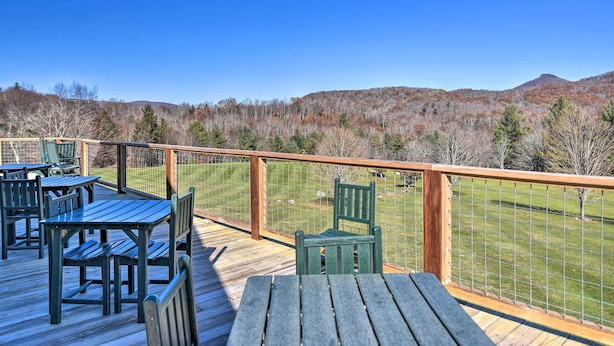 A wooden deck with tables and chairs, overlooking a grassy area and hills. - Steps to Ski Resort: Sugar Mountain Condo! (Banner Elk)