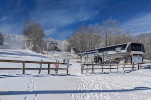 A ski resort with a wooden fence, snow-covered ground, and a ski lift in the background. - Steps to Ski Resort: Sugar Mountain Condo! (Banner Elk)