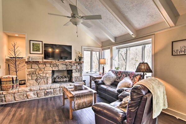 A cozy living room with a stone fireplace, leather sofa, and a flat-screen TV.