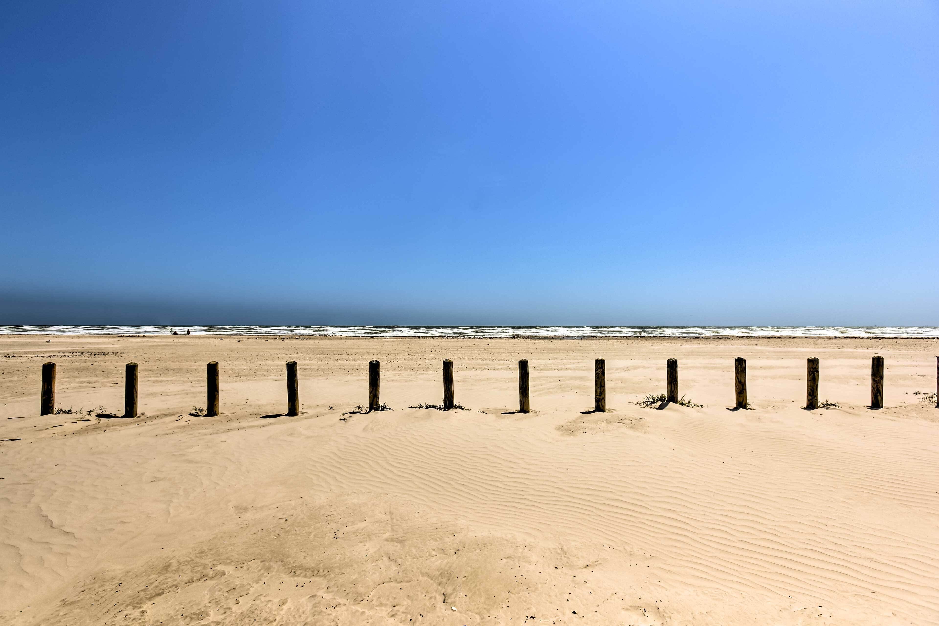 Ein sandiger Strand mit Holzpfählen im Vordergrund und dem Meer im Hintergrund.