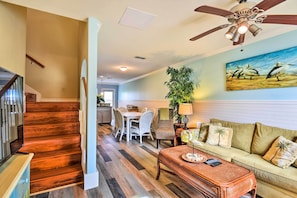 A spacious living room with a wooden staircase, a dining area, and a ceiling fan.