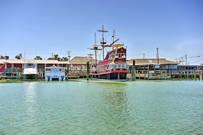 A dock with a large ship and smaller boats, wooden buildings, and a clear sky.