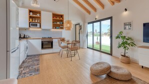Eine moderne Küche mit Holzbalken, einem Essbereich mit Korbstühlen und einer großen Glasschiebetür zum Garten.