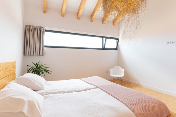 A modern bedroom with a large bed, a window, a plant, and a white chair.