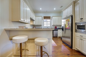 A kitchen with white cabinets, stainless steel appliances, and two white bar stools. - Large, Elegant Home < 2 Miles to Ole Miss! (Oxford)