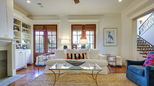 A spacious living room with a white sofa, a glass coffee table, and a blue armchair. There is a fireplace, a bookshelf, and a staircase with a railing. - Hector's Hotty Toddy: 2 Mi to Ole Miss (Oxford)