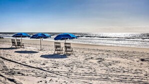 Une plage avec trois parasols bleus et deux chaises en bois.